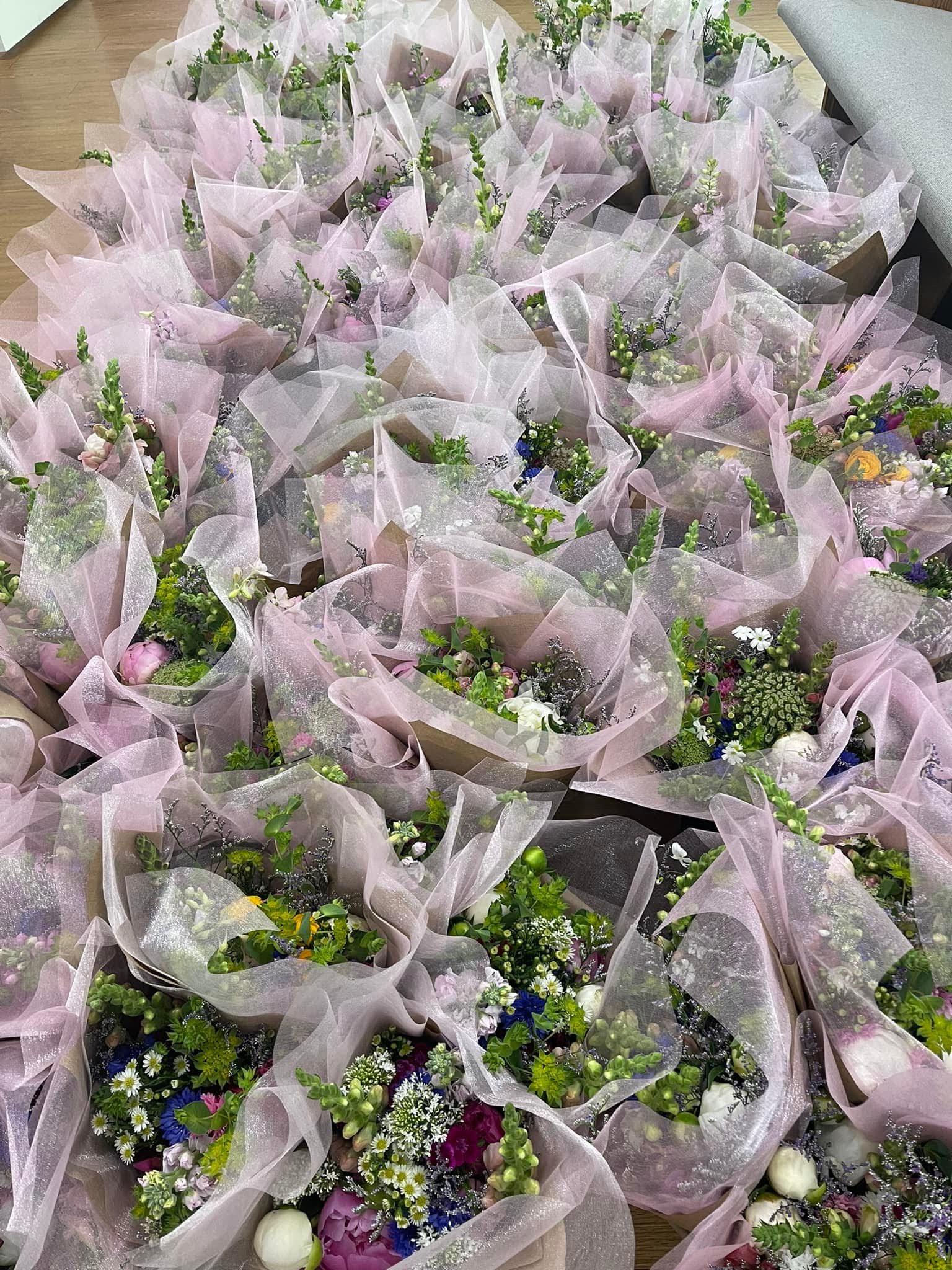 Numerous flower bouquets wrapped in light pink translucent paper are arranged closely together, featuring a mix of colorful blooms and greenery.
